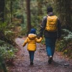 Father and daughter walking in the woods holding hands.