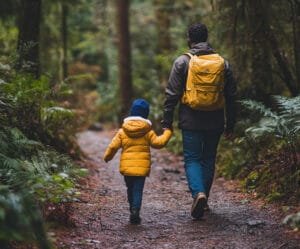 Father and daughter walking in the woods holding hands.