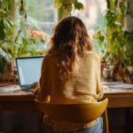 Woman sitting at a desk with her laptop in a bright, peaceful room overlooking nature through a large window, bathed in soft morning light — representing clarity and focus in the Mulry Method.