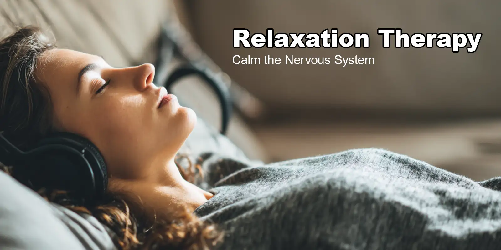 Woman lying back on a couch wearing headphones, peacefully listening during golden-hour light — representing Relaxation Therapy practice.